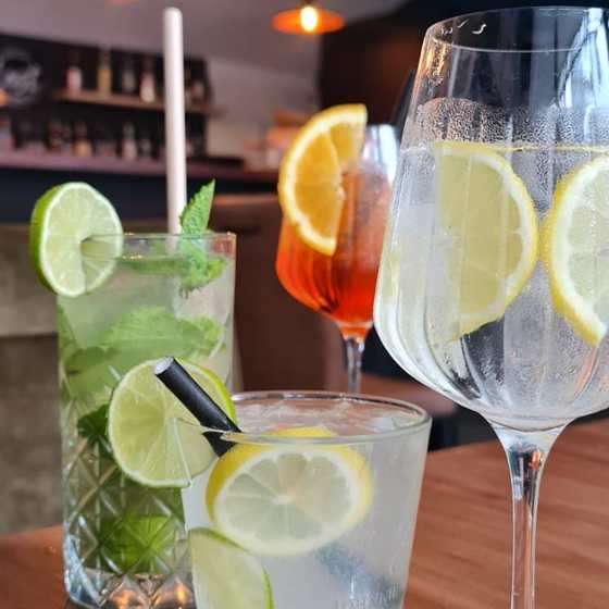 Three drinks together: Mojito, Aperol Spritz, gin and tonic in a wine glass, plus a tumbler gin and tonic, bar behind.