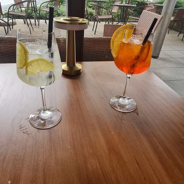 Gin and tonic and Aperol Spritz on a table by the window, courtyard with parasols and greenery outside.