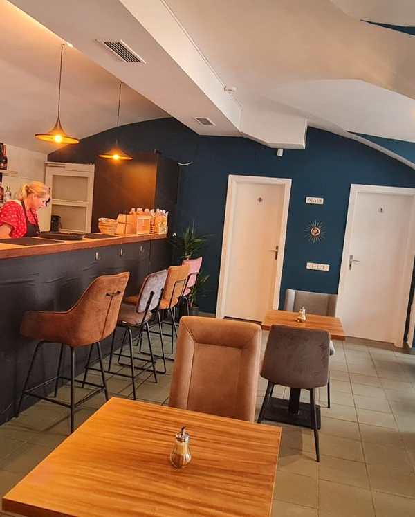 Interior, 2024: bar counter with stools and pendant lamps, blue walls, two white doors, small tables.